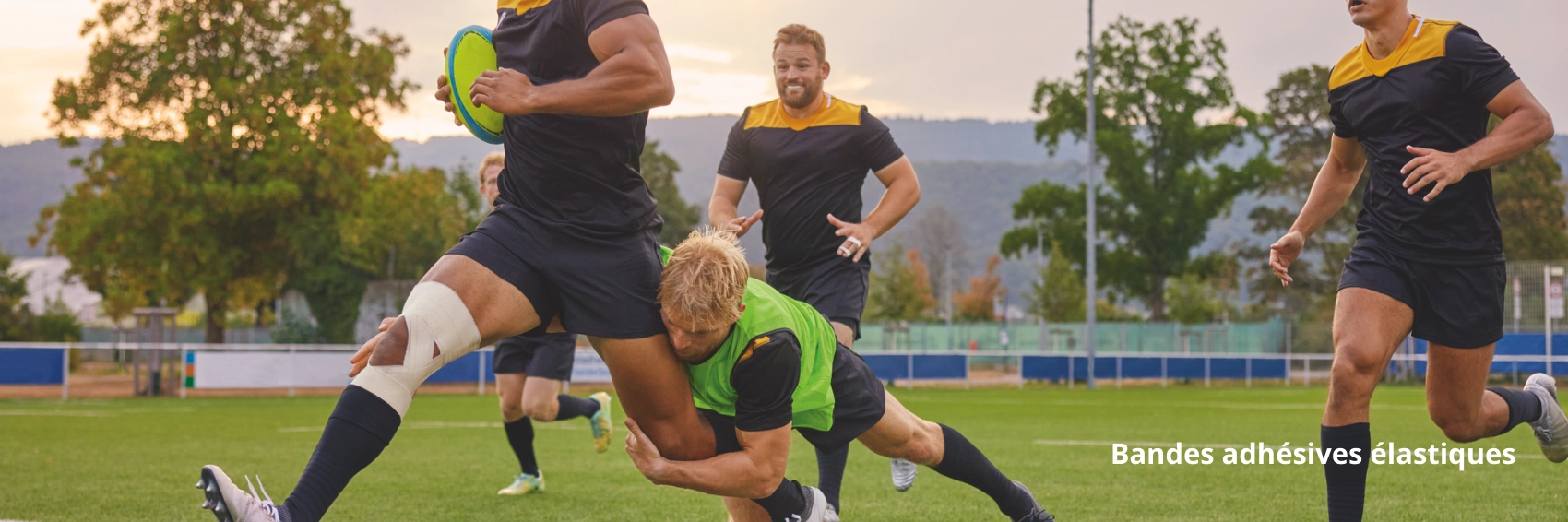  Joueur de rugby avec une bande adhésive élastique sur la cuisse, poursuivi par des adversaires pendant un match.